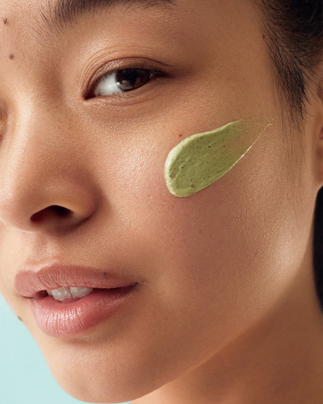Woman with green swatch of skincare product on cheek